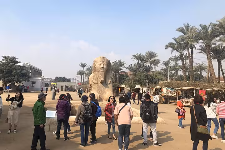 Tourists at Memphis open-air museum with colossal sphinx statue, part of Giza Pyramids Saqqara tour