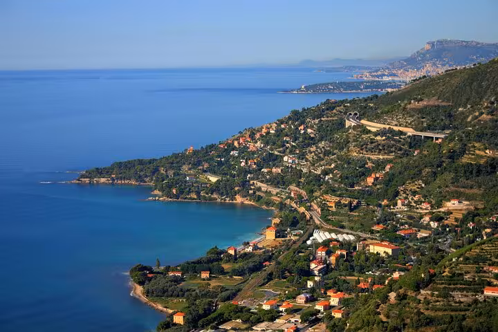 Aerial view of Menton coastline with turquoise Mediterranean sea, hillside villas, and winding coastal road