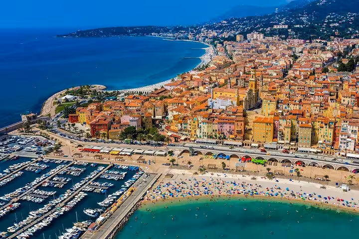 Aerial view of Menton coastal town with colorful buildings, marina with boats, and beach on French Riviera