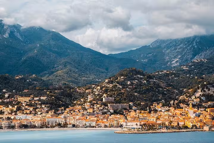 Colorful coastal town of Menton with orange-roofed buildings, turquoise sea, and green mountains backdrop
