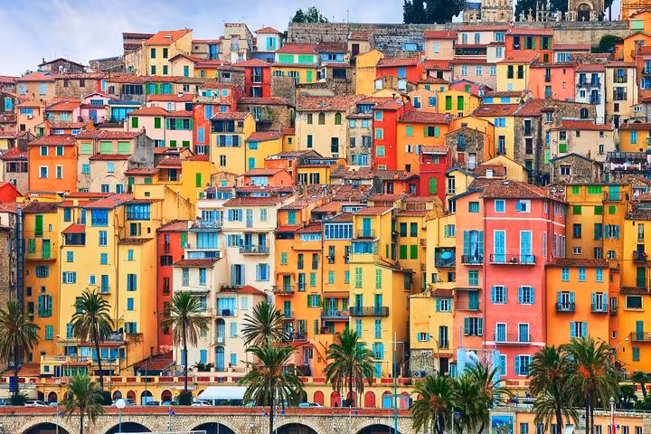 Colorful stacked buildings with terracotta roofs and palm trees in Menton, French Riviera