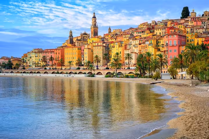 Colorful buildings and church tower of Menton old town reflected in calm Mediterranean Sea waters