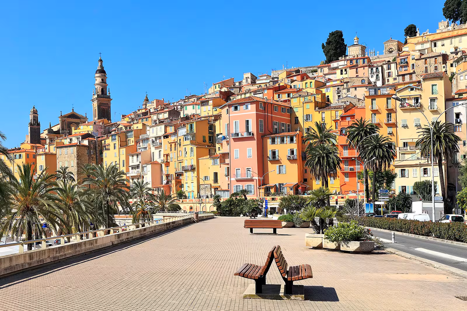 Colorful buildings of Menton old town with palm-lined promenade and church towers on French Riviera