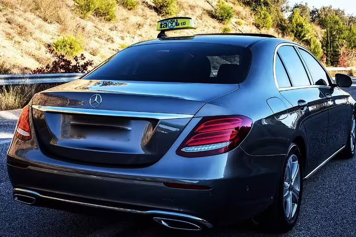 Dark grey Mercedes-Benz sedan taxi with roof sign on a road surrounded by hills