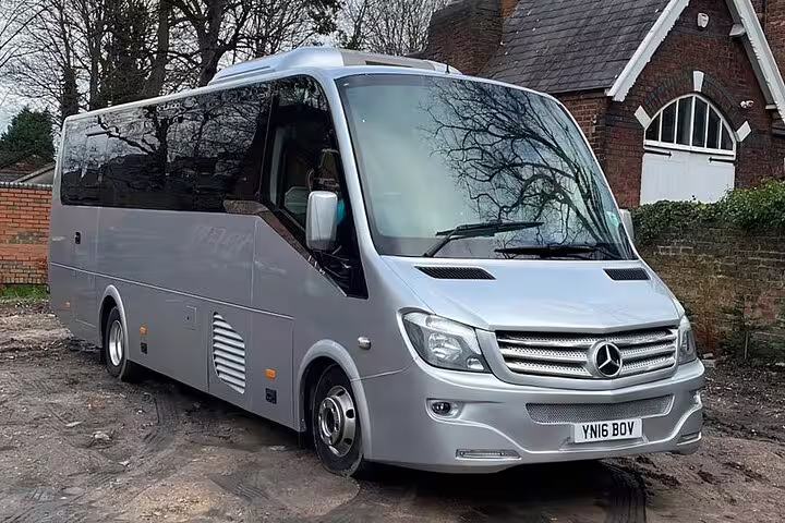 Silver Mercedes-Benz luxury minibus coach parked outside brick building, UK registration plate