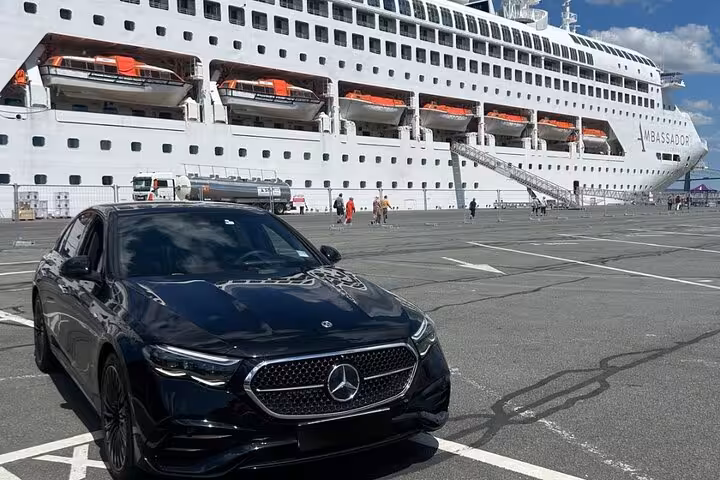 Black Mercedes-Benz sedan parked at cruise ship terminal with Ambassador cruise ship in background