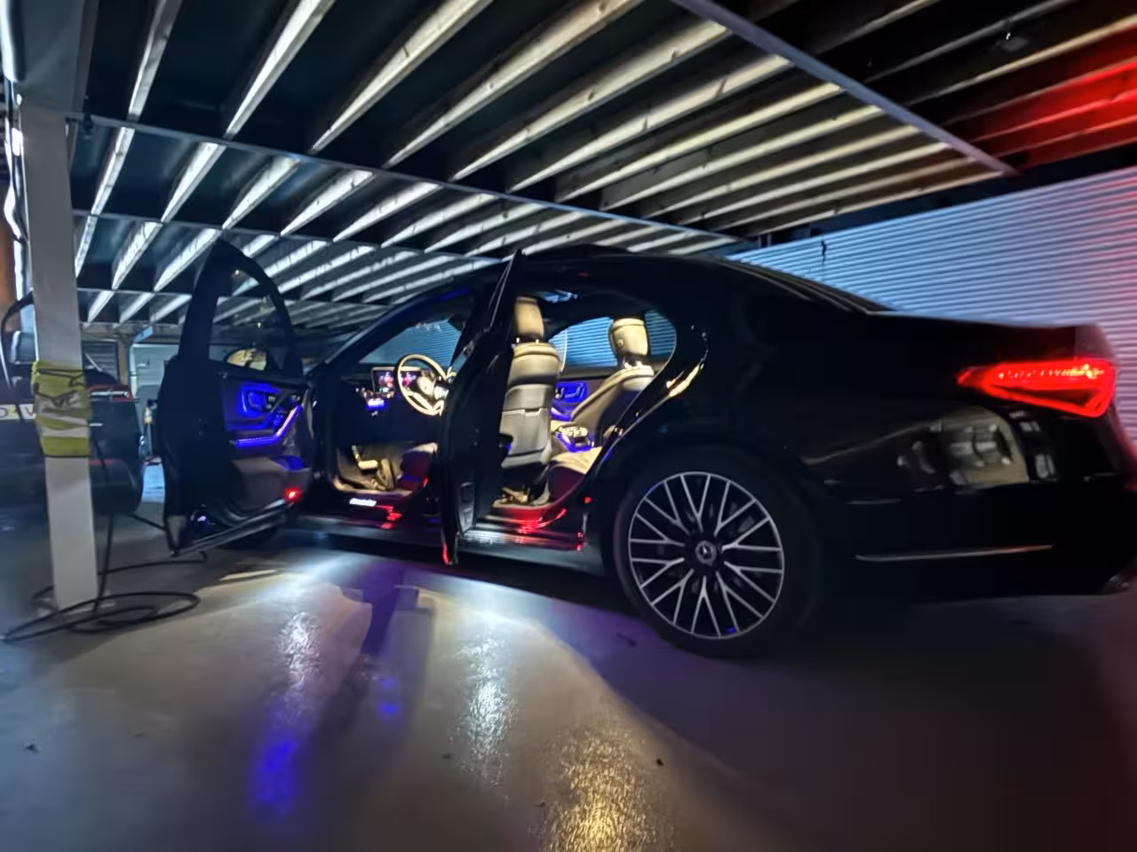 Black Mercedes luxury sedan with open doors and ambient blue interior lighting in garage