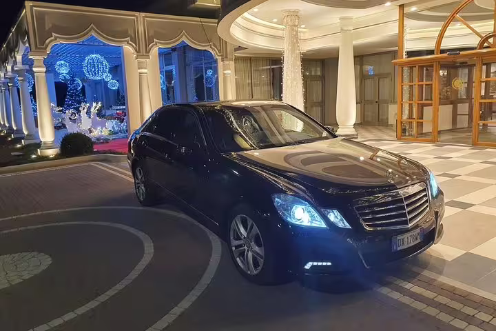 Dark blue Mercedes-Benz E-Class sedan parked at luxury hotel entrance with Christmas decorations at night