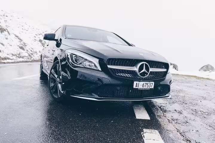 Black Mercedes-Benz CLA on wet mountain road with snowy backdrop