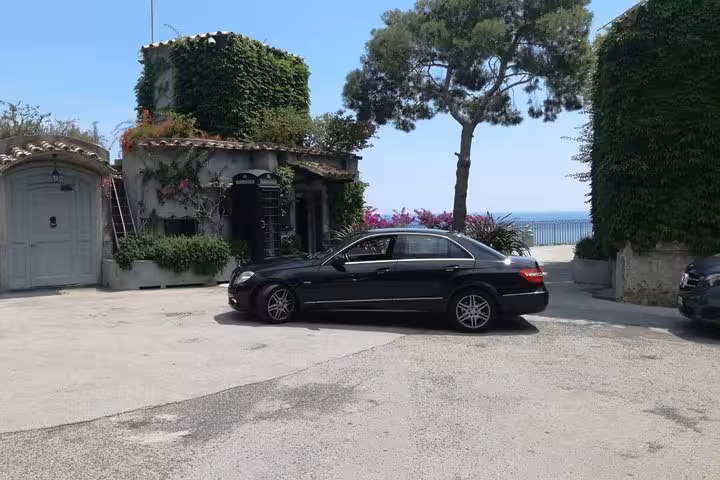 Elegant black Mercedes sedan parked by a charming villa with ocean views, perfect for Positano transfers.