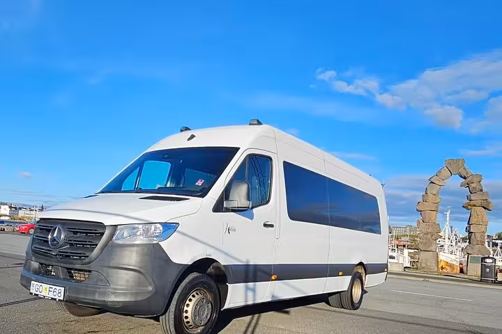 White Mercedes Sprinter minibus parked near Reykjavik harbor with stone arch landmark under blue sky