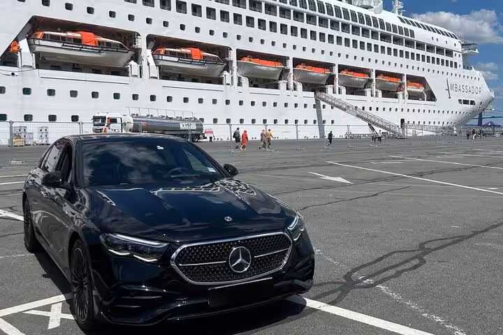 Black Mercedes-Benz sedan parked at Le Havre cruise port with Ambassador cruise ship in background