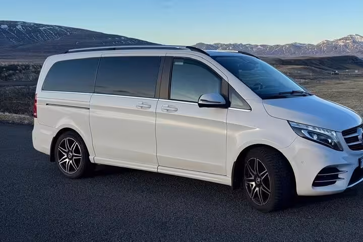 White Mercedes-Benz V-Class luxury van parked on road with snow-capped mountains in background