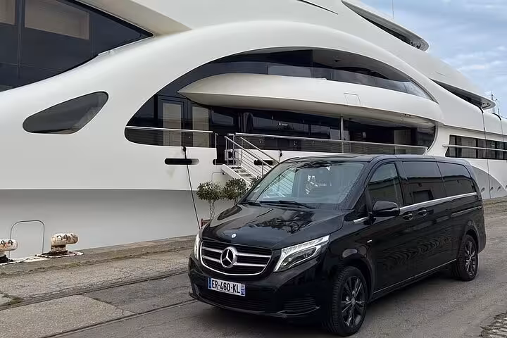 Black Mercedes-Benz V-Class van parked in front of a luxury yacht at a marina