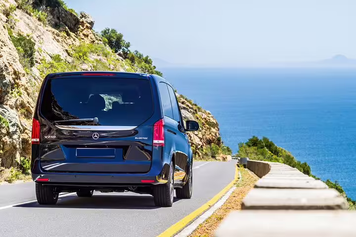Dark blue Mercedes-Benz V250 van driving along a scenic coastal road with blue sea views
