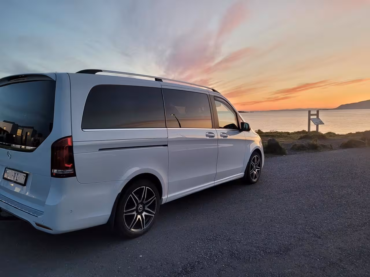 White Mercedes-Benz V-Class minivan parked near Reykjavik coastline at sunset for private airport transfer