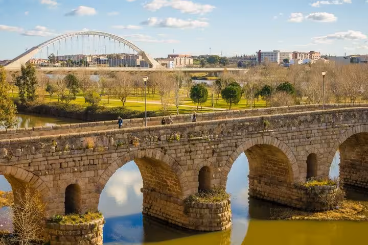 Ancient Roman bridge with stone arches over river in Mérida, Spain, with modern arch bridge in background