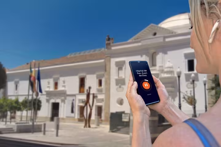 Tourist using smartphone audio guide app in front of Hospital de San Juan de Dios in Merida, Spain