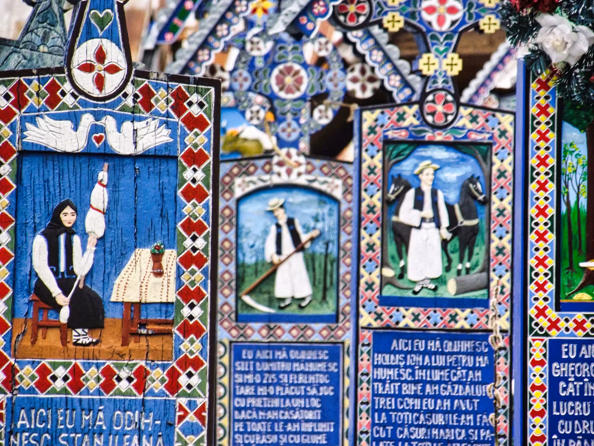 Colorful hand-painted wooden crosses with folk art scenes and Romanian inscriptions at Merry Cemetery, Maramures