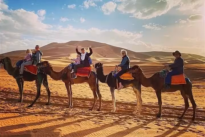 Tourists enjoying a camel ride at sunset across the golden dunes of the Merzouga Desert.