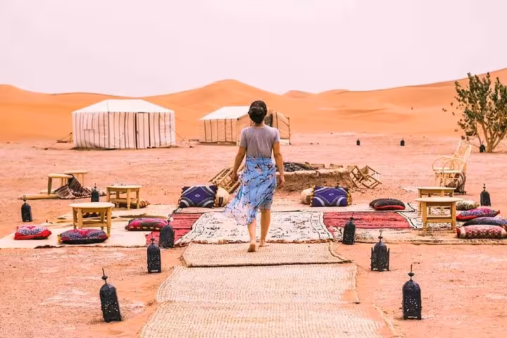 Guest approaches a cozy desert camp setup in Merzouga during a 3-day tour from Fes, surrounded by scenic dunes.
