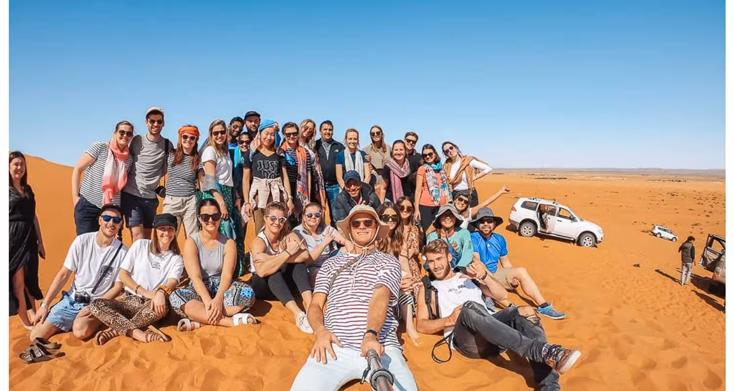 Group of tourists enjoying a sunny day on the Merzouga Desert safari with off-road vehicles in the background.