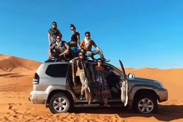 Group enjoying a thrilling Merzouga desert tour, perched on a 4x4 amidst expansive sandy landscapes.