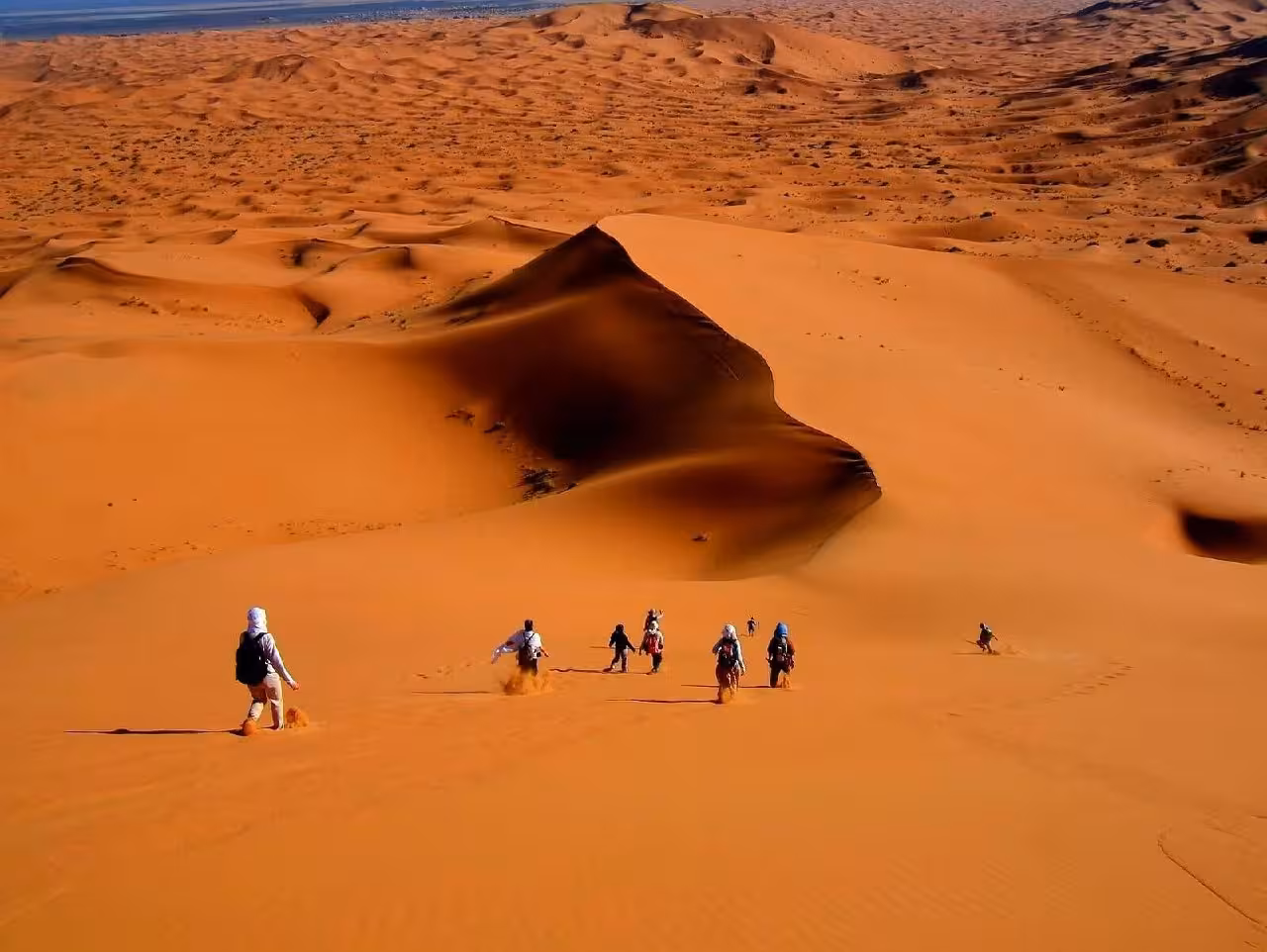 Travelers trek down the expansive sand dunes of Merzouga Sahara, experiencing the unique landscapes on a desert tour.