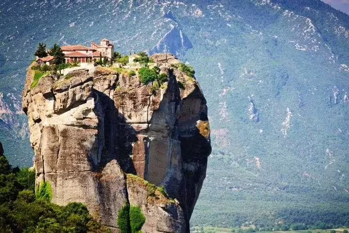 Scenic view of a Meteora monastery perched atop a towering rock formation surrounded by lush landscapes.