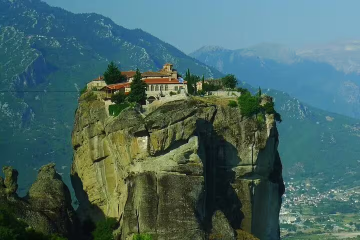 Meteora hilltop monastery on massive sandstone cliff with mountain backdrop, Athens to Meteora private day trip