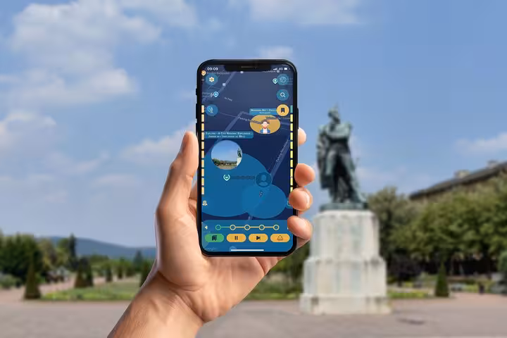 Hand holding smartphone with self-guided walking tour app in front of bronze statue in Metz, France