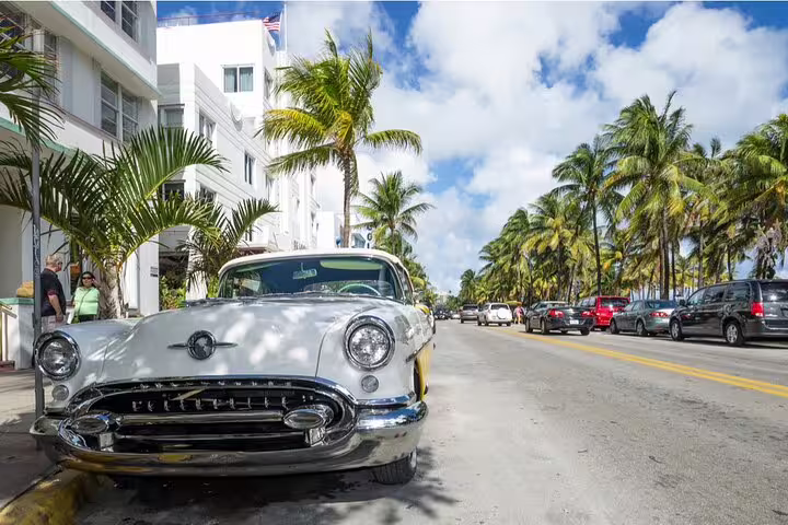Classic vintage car parked on Miami Beach's Ocean Drive lined with palm trees and Art Deco buildings