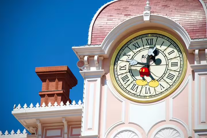 Mickey Mouse clock tower at Disneyland Paris with pink facade and blue sky