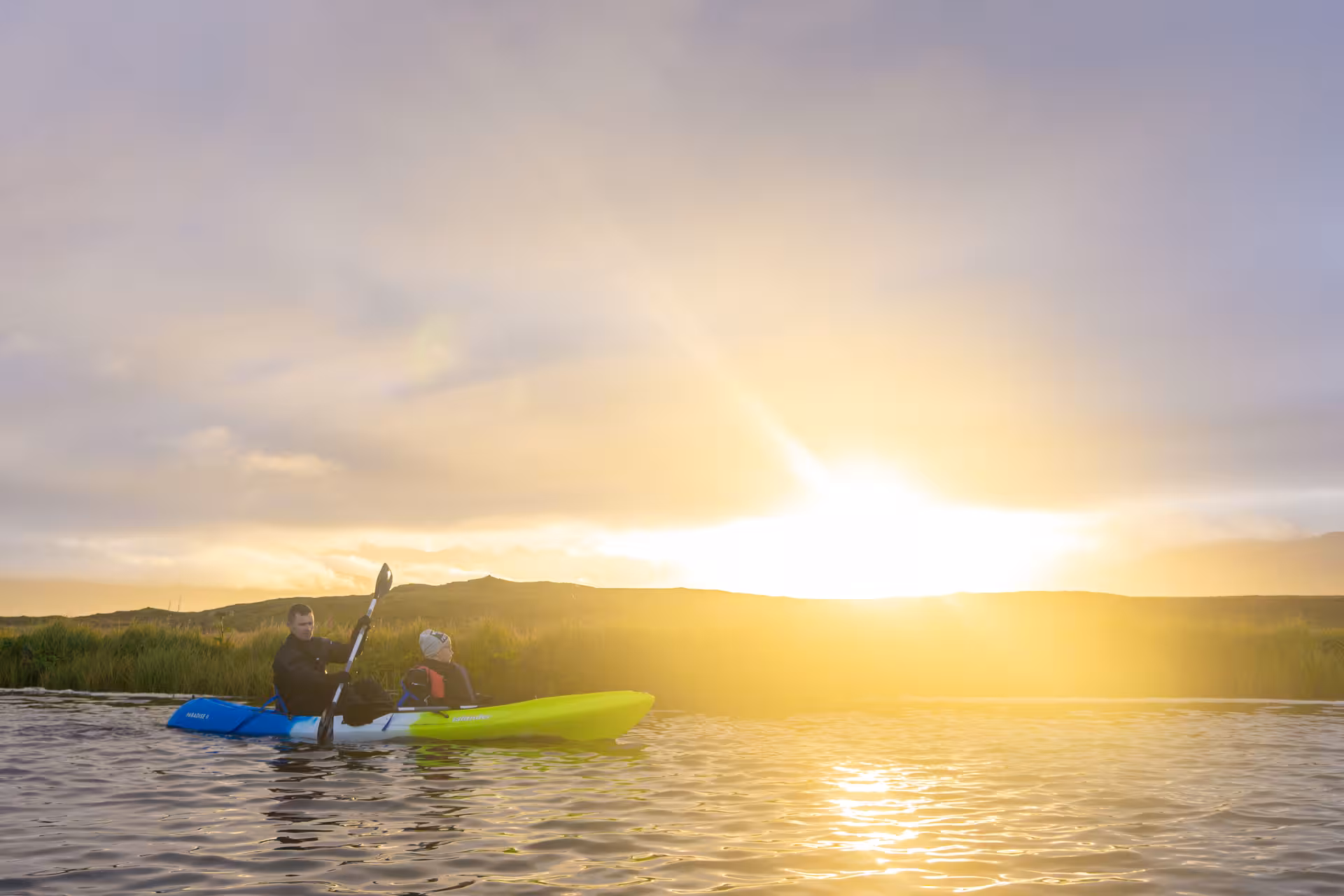 Two kayakers enjoy a serene midnight tour under a glowing sunset on tranquil waters.