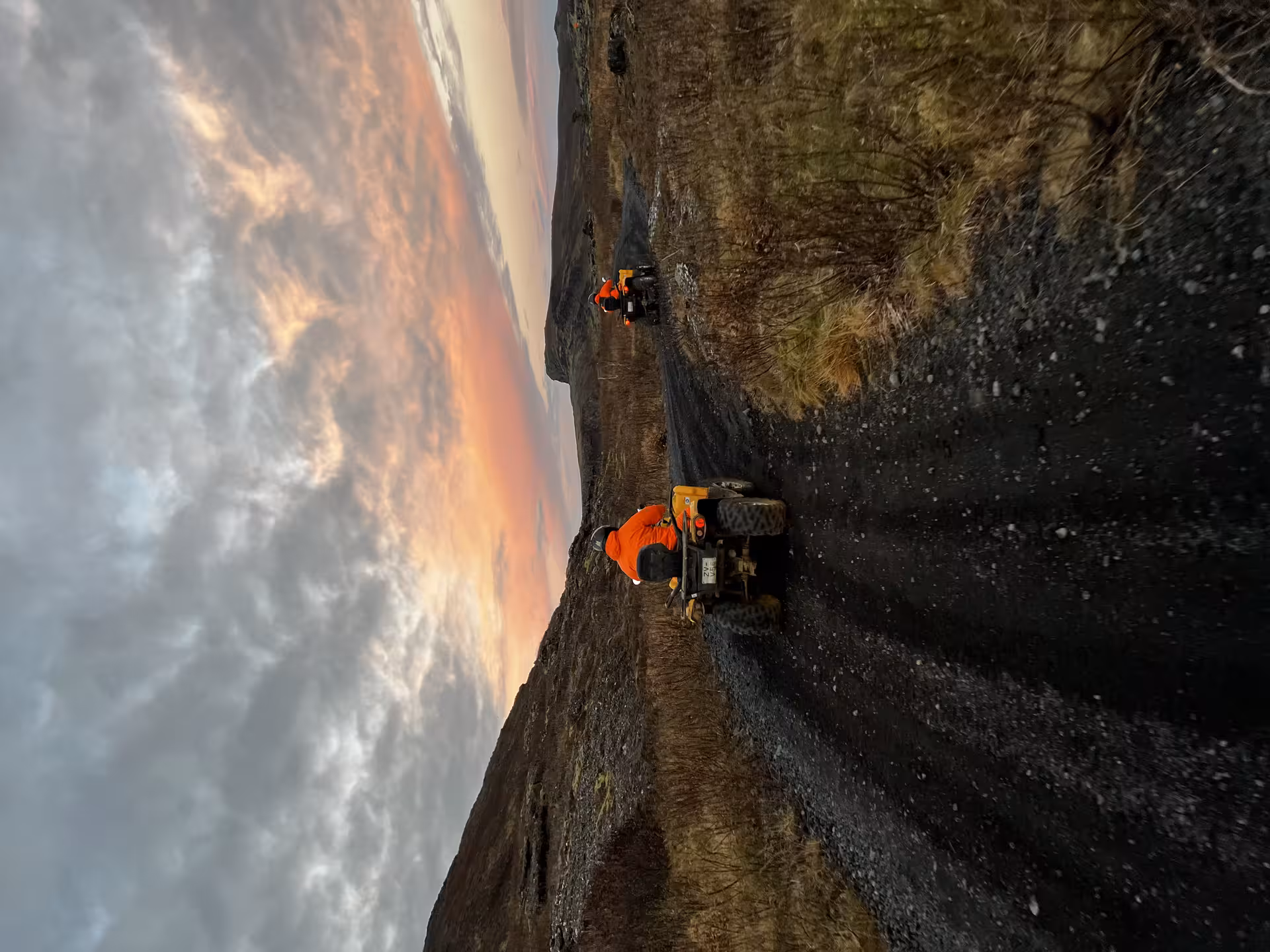 Two riders in orange gear on ATVs crossing black lava fields at sunset in Reykjanes, Iceland