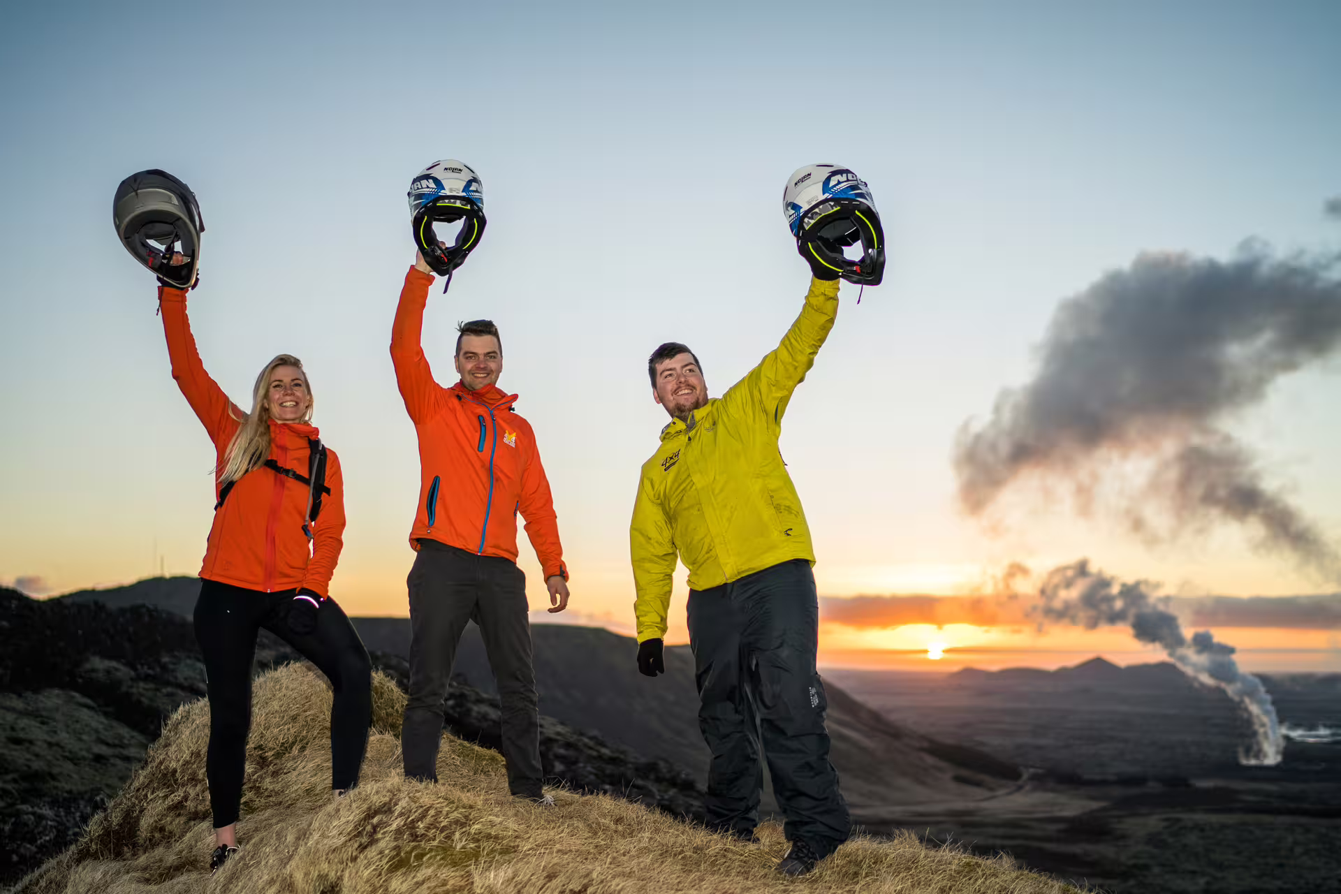 Three adventurers raising ATV helmets at sunset on Reykjanes volcanic lava fields Iceland