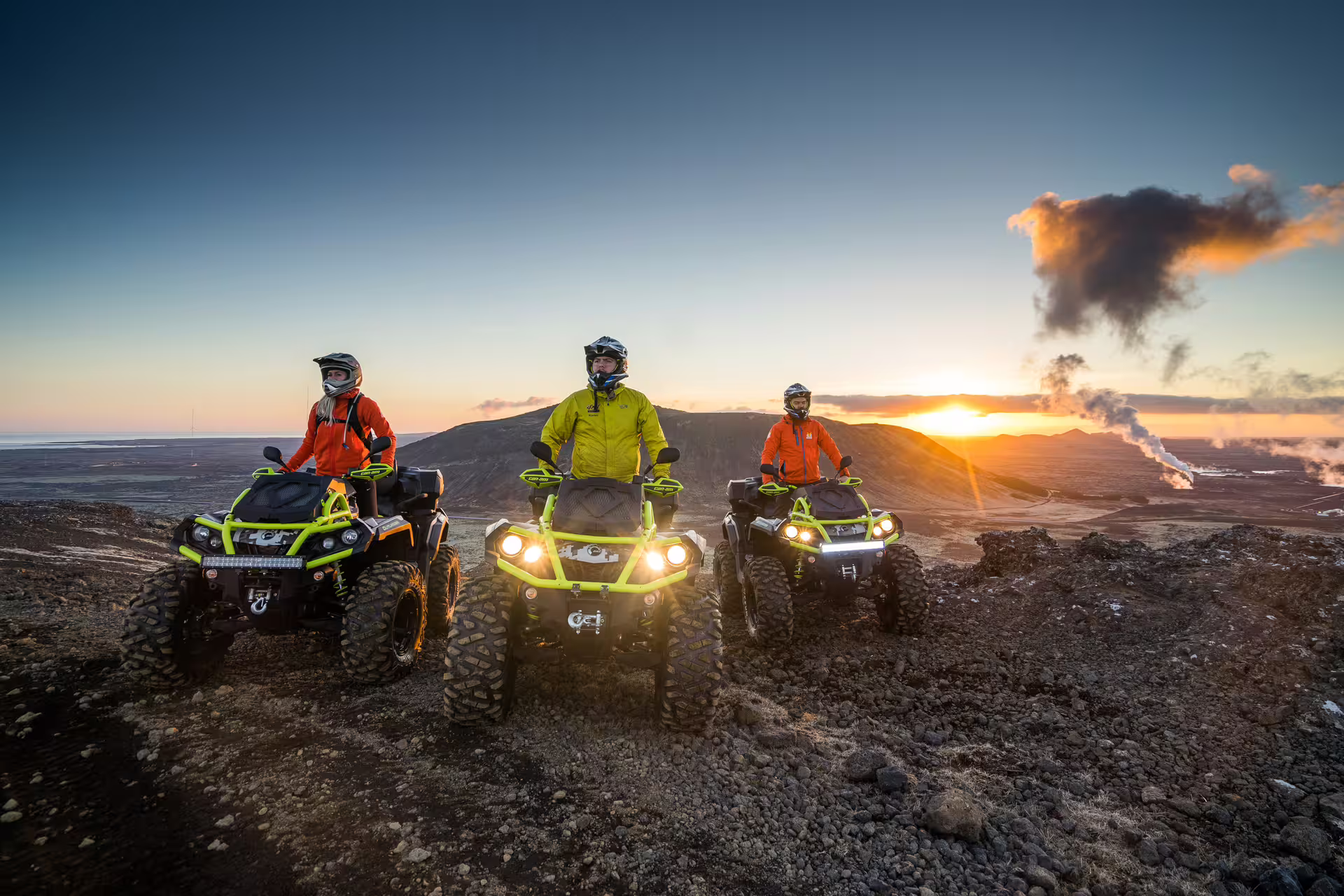 Three riders on neon ATVs pause on volcanic lava fields in Reykjanes Iceland at sunset