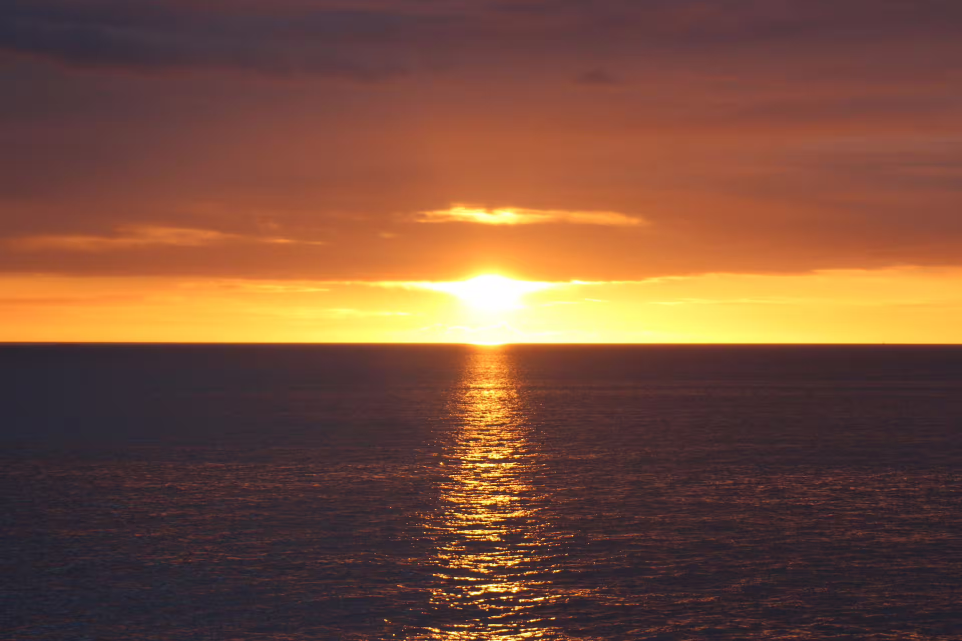 Golden midnight sun setting over calm ocean horizon in Reykjavik, reflecting light on water