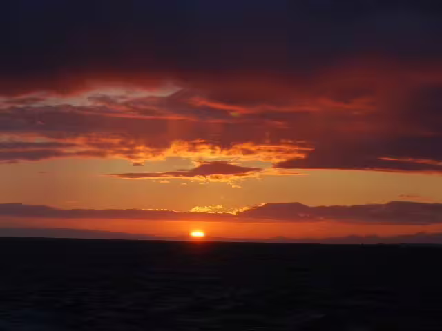 Midnight sun setting over the ocean horizon with dramatic orange and red clouds from Reykjavik