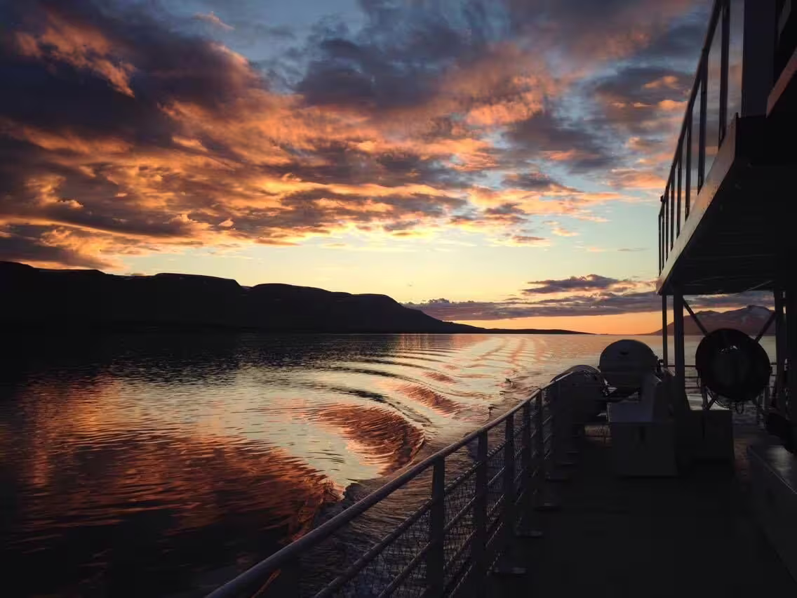 Sunset view from the stern of a whale watching boat sailing through calm fjord waters near Akureyri