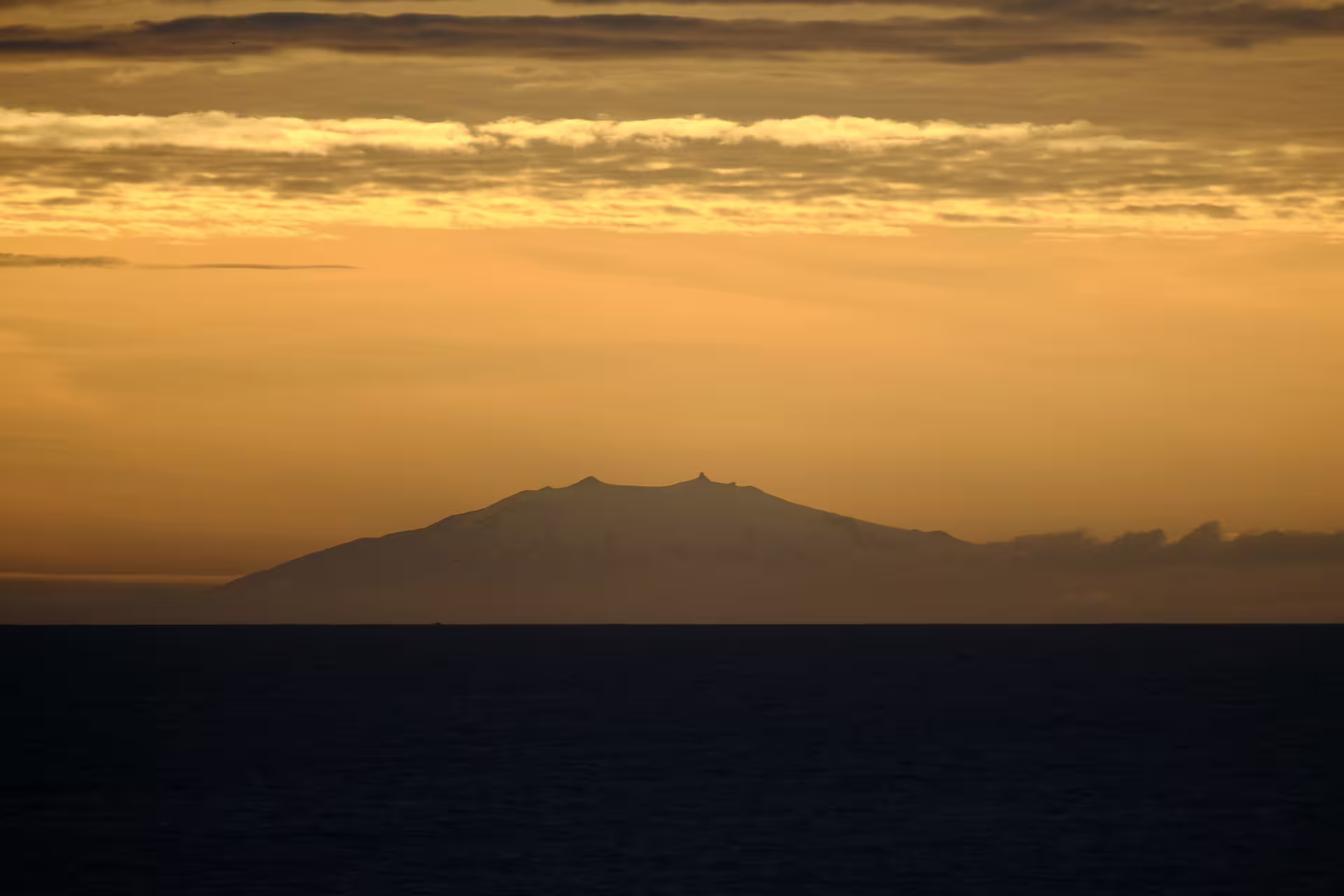 Volcanic island silhouette over dark ocean under golden midnight sun sky in Reykjavik