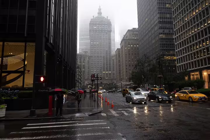 Rainy Midtown Manhattan street with yellow taxis and pedestrians with umbrellas on a foggy day