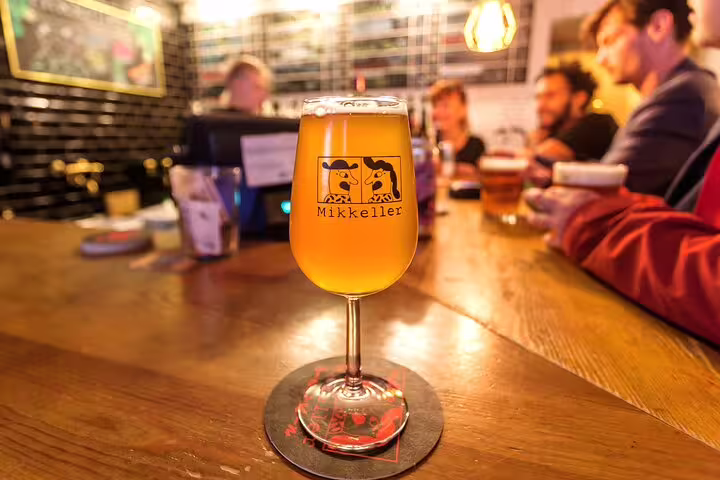 Glass of Mikkeller beer on a wooden bar surrounded by people enjoying the Copenhagen Food & Drink Private Tour experience.