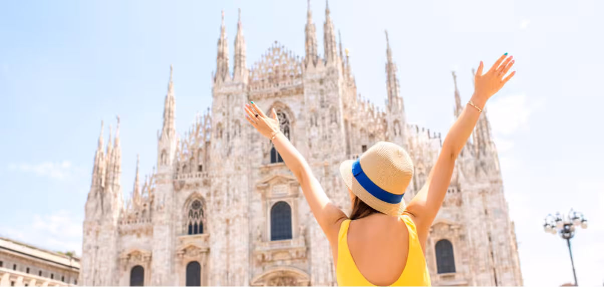 Joyful tourist raises arms in front of Milan Cathedral on guided tour with skip-the-line access to La Scala Theatre.