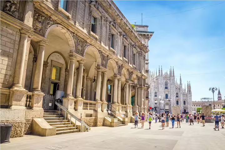 Tourists walking in Piazza del Duomo Milan with Gothic cathedral and historic colonnade building
