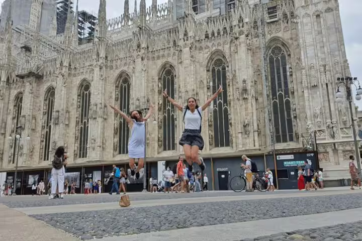 Two women jumping joyfully in front of Milan Cathedral Duomo during a self-guided walking tour