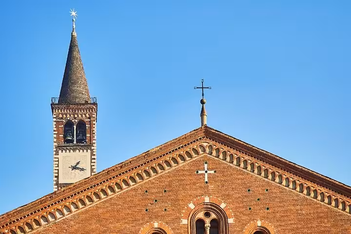 Historic brick church facade and bell tower with cross in Milan Navigli district under blue sky