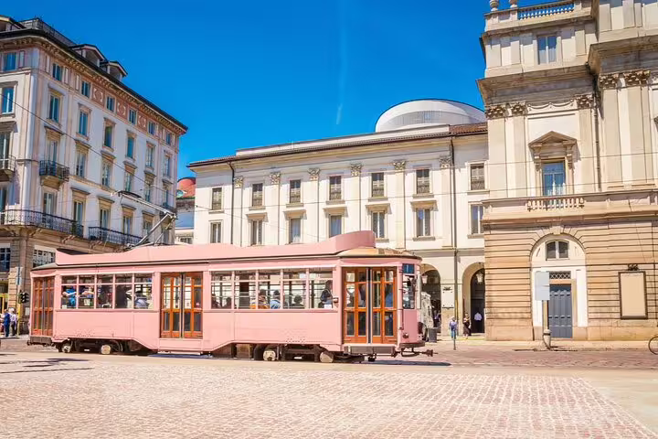 Pink vintage tram on cobblestone piazza in Milan with neoclassical buildings under blue sky