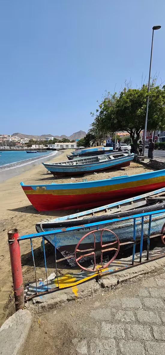 Colorful fishing boats rest on the sandy shores of Mindelo, São Vicente, offering a glimpse of local culture and stunning coastal views.