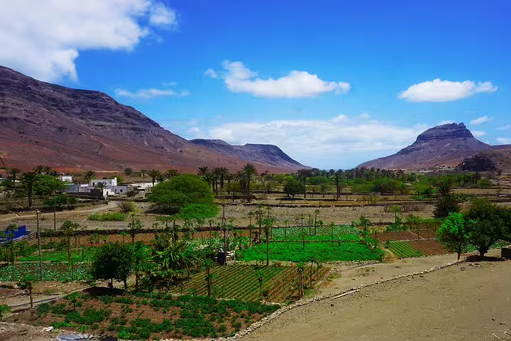 Lush green fields surrounded by rugged mountains under a clear blue sky, showcasing Mindelo's stunning natural landscapes.